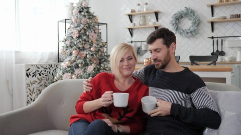 Festive mood, Christmas or New Year, a young couple sitting on the couch and drinking hot tea. Christmas decor and beautiful room.