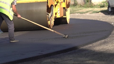 A cargo dump truck pours asphalt concrete mixture into a paver hopper for road repair