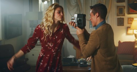 Cinematic shot of an young transgender man is filming with vintage camera his carefree happy smiling homosexual female gay partner while is having fun and dancing crazy at home.