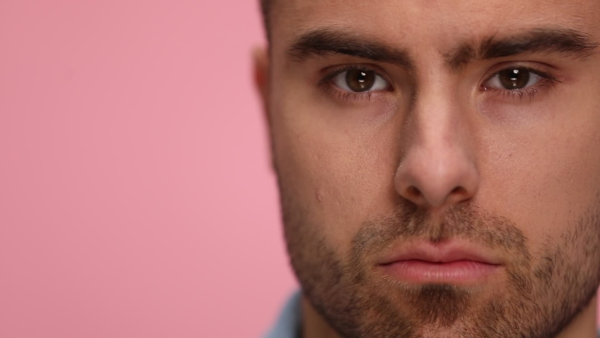 close up of attractive young man in blue shirt raising eyebrows, moving head and posing on pink background in studio.