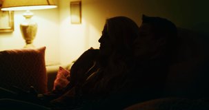 Cinematic shot of young carefree happy smiling homosexual female gay and transgender man couple in love is having fun watching television while lying on a sofa in living room at home at night.