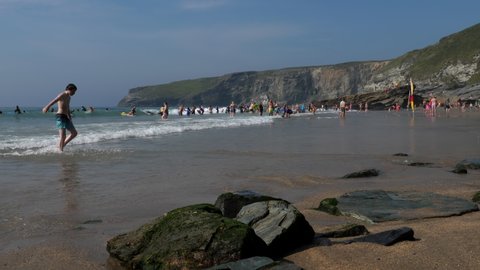 CORNWALL, ENGLAND, UNITED KINGDOM - CIRCA AUGUST, 2020: Young people enjoying sea waves at a beautiful Trebarwith beach on a sunny summer day.