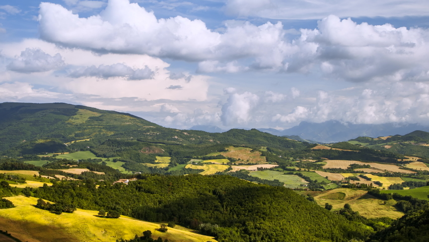 Beautiful summer day timelapse with moving cloud shadows over green forest trees, hills, rural fields and meadows, sunny nature outdoor landscape panorama scenery in Italy. Blue sky background 