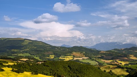 Beautiful summer day timelapse with moving cloud shadows over green forest trees, hills, rural fields and meadows, sunny nature outdoor landscape panorama scenery in Italy. Blue sky background 
