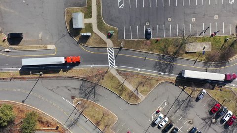 A top down shot over two trucks pulling in to a truck stop on a sunny day. The drone camera, pointing straight down, truck right following them as they prepare to park.