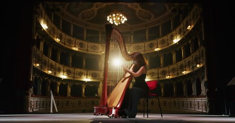 Cinematic shot of professional female harpist wearing protective medical mask is playing harp solo on a classic theater stage with dramatic lighting before start a music concert.