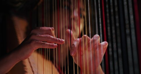 Cinematic close up shot of professional female harpist is playing harp solo on a classic theater stage with dramatic lighting before start a music concert.