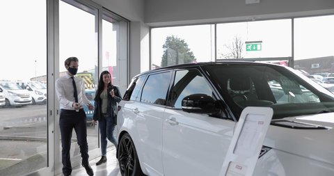 Car salesman showing customer car in automotive dealership showroom
