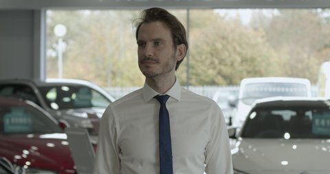 Portrait of car salesman looking at camera in automotive dealership showroom