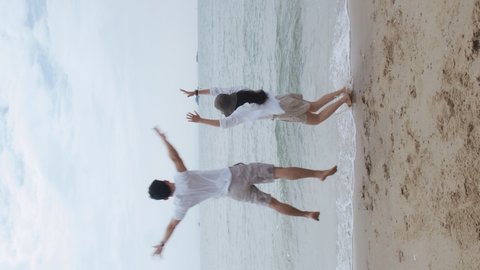 Vertical Video: Asian couple in love running jump celebrating success with raised arms into the air on the holiday weekend. Romantic couple on the beach vacation travel.