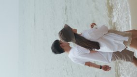 Vertical Video: Happy asian couple walking at the seaside and enjoying on vacation summer, happy talking and laughing, and look at the view on the beach.