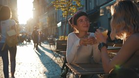 Two attractive caucasian girls sitting at the street cafe at pleasant sunset drinking juice or coffee, communicate and sharing stories while drinking orange juice, spending relax outdoor evening. - Powered by Shutterstock - Get 15% off with code: PIKWIZARD15