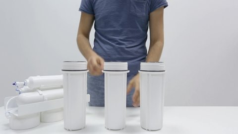 Male hands show carbon partially permeable membrane cartridges inside cylinders of reverse osmosis household water filter