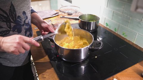 Womens hands mashing patato in pan on kitchen hob, cooking mash potato