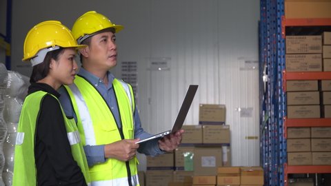 asian warehouse manager holding laptop computer training to  trainee worker woman controlling stock and checking list inventory in warehouse factory. New employees learn to work from supervisor. 