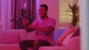 Relaxed carefree smiling african man using smartphone for videochat taking selfies recording video message in living room. Neon illumination. Carefree lifestyle. Technology.