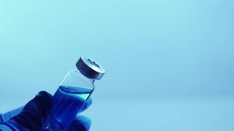 Vaccine and infectious disease developing concept. Doctor holding sterile vial with blue medication against coronavirus, COVID-19. Clinical trials development and testing on human depiction.
