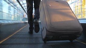 Feet of successful businessman walking in hall of terminal with his luggage. Legs of wealthy businessman walking escalator and pulling suitcase on wheels. Concept of business trip. Slow mo Back view - Powered by Shutterstock - Get 15% off with code: PIKWIZARD15