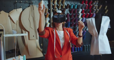 Portrait of woman fashion clothing designerin small studio wearing vr headset designing and modeling clothes using innovations technologies. Female tailor in atelier in virtual reality glasses