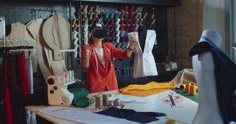 Woman clothes designer standing in workshop using VR headset and designing collection. Female professional in atelier work wearing virtual reality glasses. Futuristic innovation in fashion industry