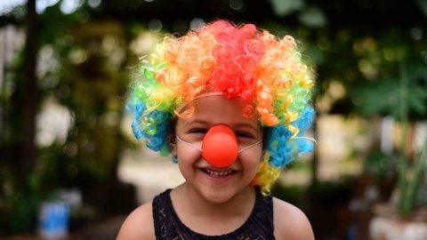 Little Brazilian girl dressed as a clown and playing happily, blurred background, selective focus.