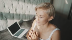 Young blonde woman praying or meditating in her bedroom. Online meditation session