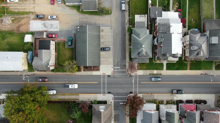Aerial top down tracking shot of car driving on street. American small town USA establishing shot of houses along road. Colorful autumn trees in Northeast United States.