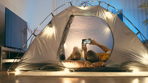 Father and son watching smartphone, talking on video call phone in tent with Christmas decorations in home. Family online chat. Long distance communication. Staying connected. 
