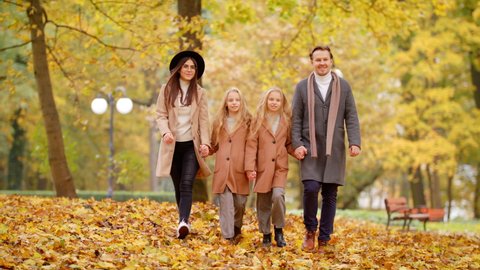 Happy Family On Autumn Walk. Mother Father and Children Twins Walking Holding Hands In The Park And Enjoying The Beautiful Autumn Nature. Friendly Family Kid Concept Autumn Countryside Slow Motion