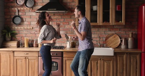 Couple dancing in cozy kitchen holding hands enjoy hobby and funny active weekend together, husband lifted wife in arms and circles spinning her in dance. Family celebrate move day to new home concept