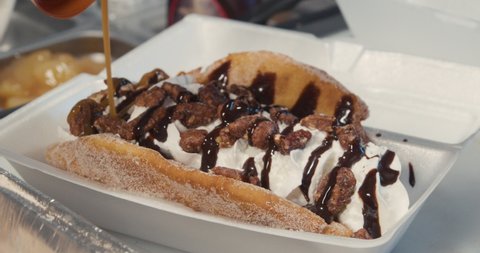 Drizzling caramel sauce on a fried ice cream dessert. Food truck serves up a decadent sweet dessert with a crunchy fried shell, ice cream, whipped cream, chocolate sauce, candied nuts and carmel sauce