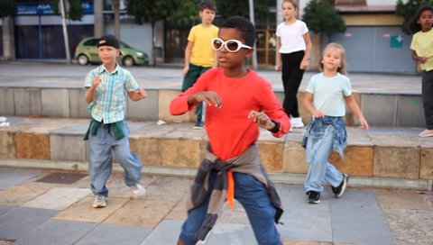 Portrait of confident african boy in sunglasses dancing hip-hop with group of tweens on summer city street. High quality FullHD footage