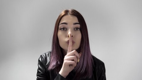 Portrait of young caucasian woman keeping a secret or asking for silence on the white background. Pretty lady brings forefinger to her lips. She makes shush movement. Theme of gesturing and signs.