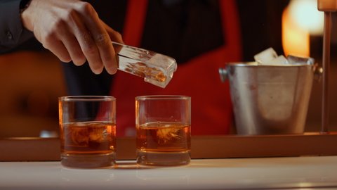 Closeup bartender hands putting ice cubes with forceps in glasses in bar. Unknown barman making drinks for party in restaurant. Unrecognizable bar man preparing whiskey for people in nightclub.
