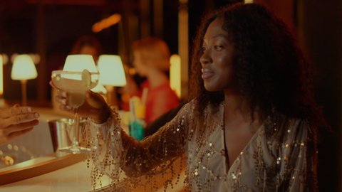 African american woman drinking cocktail at nightclub party. Closeup handsome afro man flirting with african girl in restaurant. Young couple having rest in bar at evening
