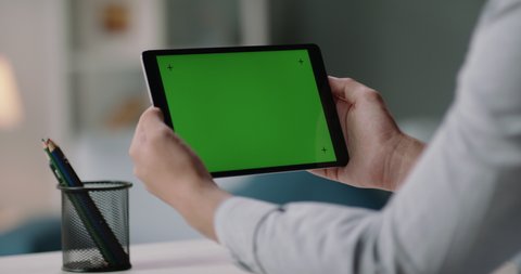 Close up shot of man holding a tablet computer with green screen. Guy working or watching a webinar, attending online video conference, staying at home. c 4k footage