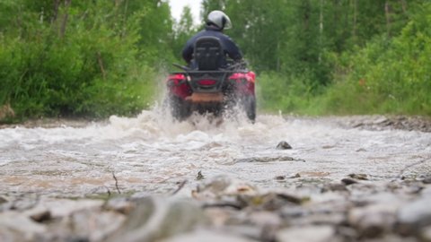 Close up ground level shot of male rider in helmet driving red four-wheeler through water