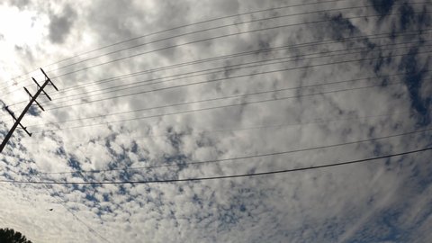 Driving along a road and looking up a the sky,clouds and utility wires and poles