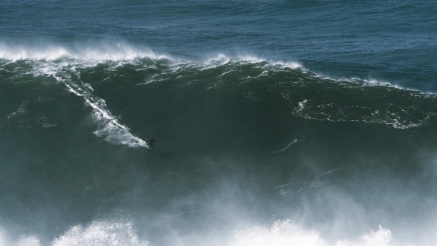 Slow motion of a big wave surfer riding one of the biggest monster waves in Nazaré, Portugal. Nazaré is a small village in Portugal with the biggest waves in the world. | Shutterstock HD Video #1061754766