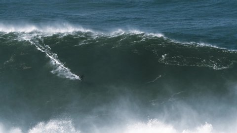 Slow motion of a big wave surfer riding one of the biggest monster waves in Nazaré, Portugal. Nazaré is a small village in Portugal with the biggest waves in the world.