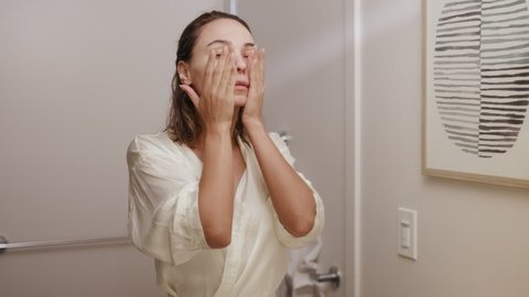 woman applying cream and scrub on her face in bathroom / skincare 