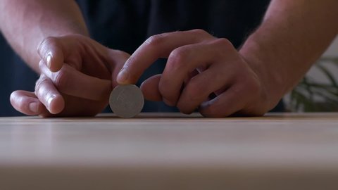Skilled man hands holding coin and hitting it to spin and bounce along wooden table, slow motion close up shot