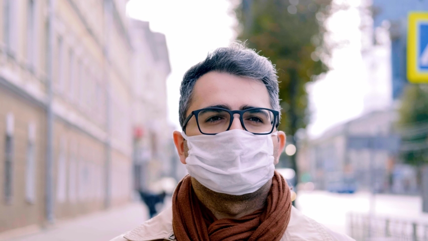 man with an Oriental appearance in a mask walks down the street along the sidewalk along the road. Protecting health in the context of the covid-19 coronavirus epidemic. Slow motion