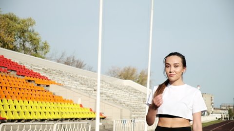 slim young fitness runner with ponytail in sportswear walking on running track. fit sportive asian female in activewear walks along statium tribune. sports, healthy lifestyle. sportswoman portrait