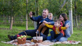 remote communication, young family with young male children communicate by video call on smartphone with their relatives while relaxing on picnic in countryside among trees
