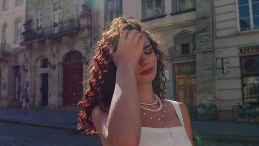 Beautiful curly brunette woman wearing pearl necklaces. Happy, smiling fashionable lady posing in sunny street European city. Royalty-Free Stock Footage #1061770642
