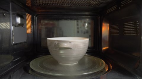 A ceramic bowl with some food is heated in the microwave, rotating