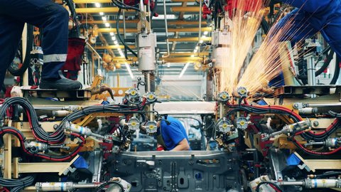 Several factory workers welding a car body at a car factory