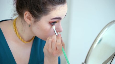 Female sitting at table and applying eyeliner with brush in the mirror