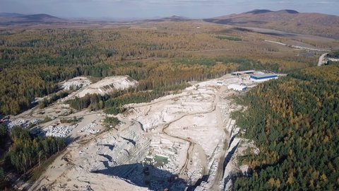 The big mine in the middle of the forest. The hills. Granite production. Long tire track following the trucks driving into the mine. A lot of the big granite blocks are placed on the ground. Aerial